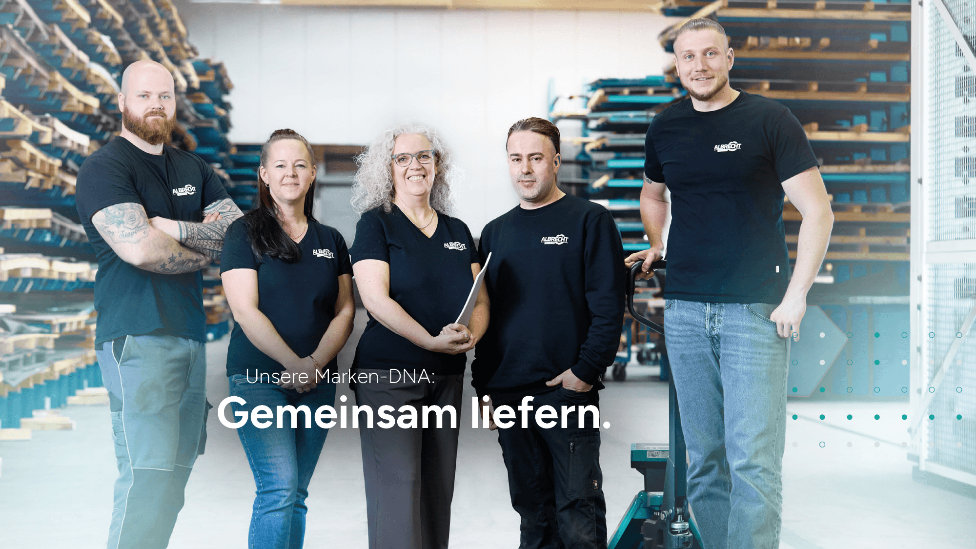 Albrecht Team im Lager Fünf Mitarbeiter von Albrecht stehen zusammen im Lager vor Regalen und lächeln in die Kamera.