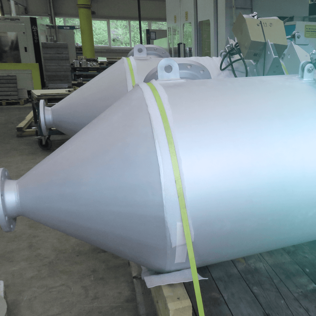 Two large, conically tapering metal cylinders with flanges inside a workshop.