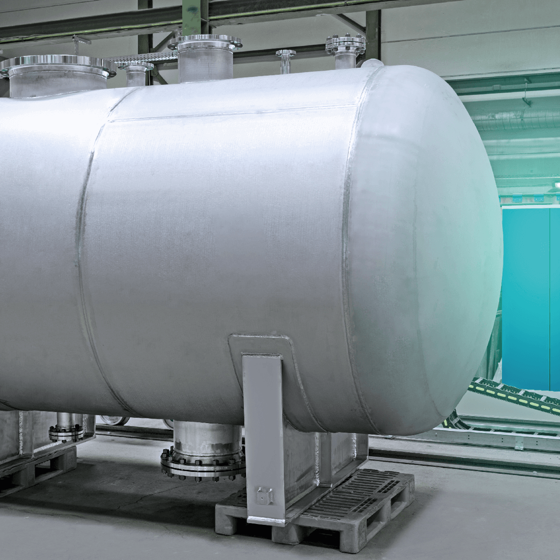 Large industrial stainless steel tank on pallets in a bright production hall with greenish lighting.