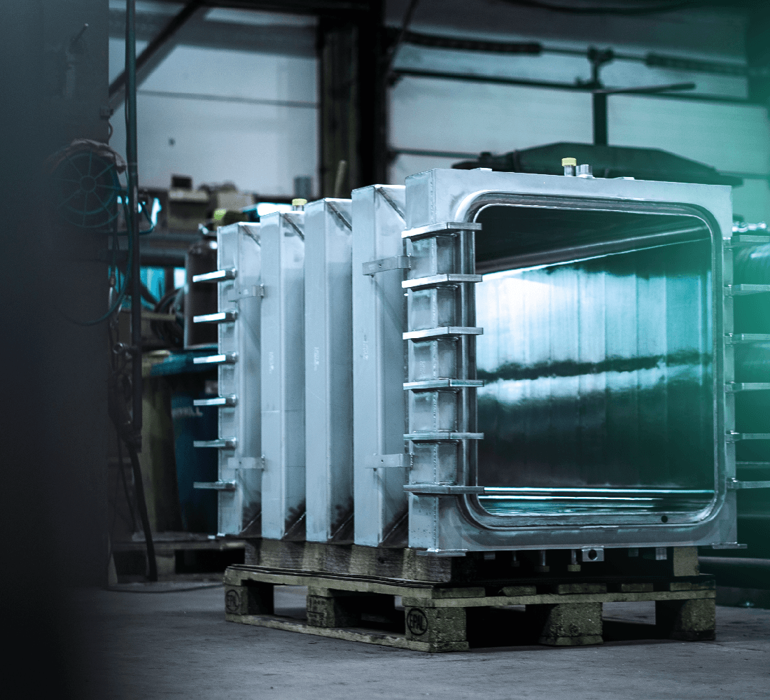 Several shiny stainless steel radiator components stand on a Euro pallet in an industrial hall.