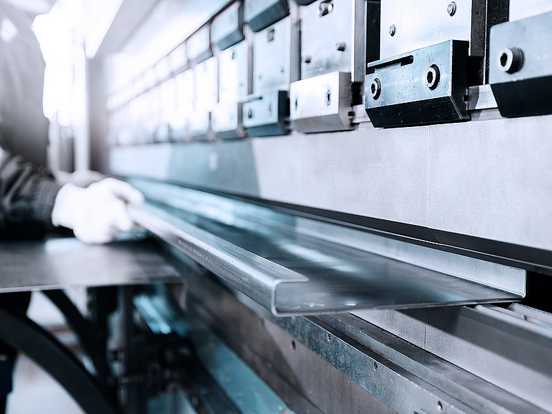 Worker bending a metal sheet using an industrial press brake.