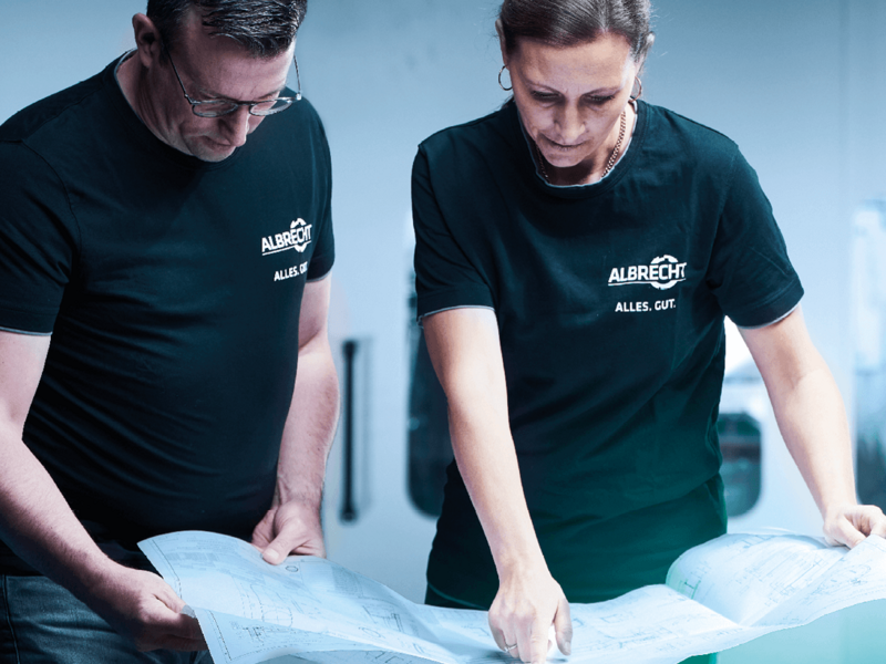 A man and a woman in matching shirts with the Albrecht logo look at and discuss a large construction plan.