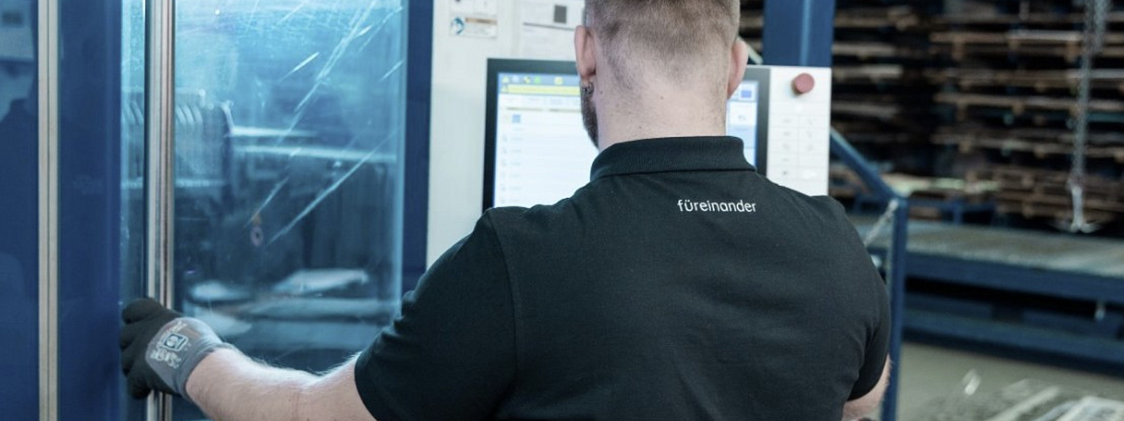 Ein Arbeiter mit schwarzem Poloshirt bedient eine moderne CNC-Maschine in einer Produktionshalle.