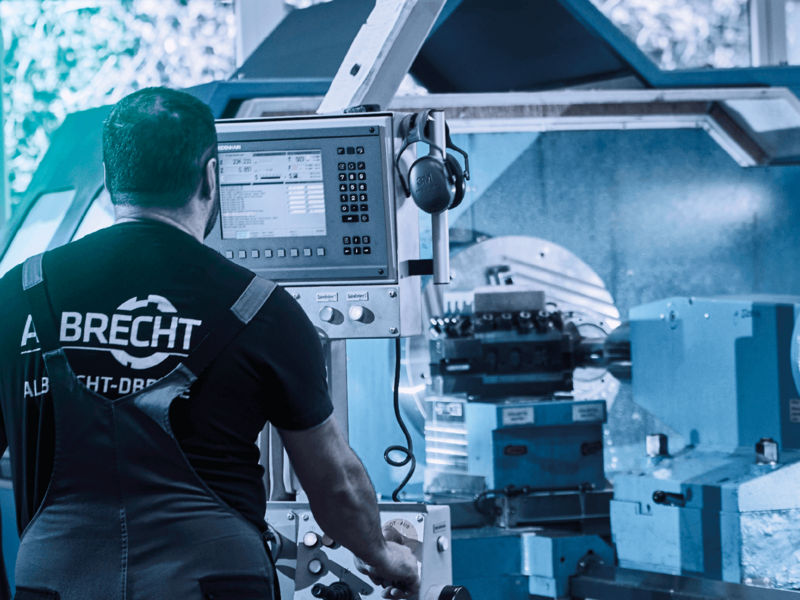Mitarbeiter in Arbeitskleidung bedient eine moderne CNC-Drehmaschine in einer Werkstatt.