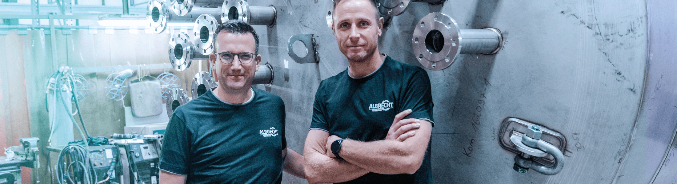 Zwei Männer in dunklen Shirts stehen in einer Werkstatt vor einem großen Industrietank aus Edelstahl.