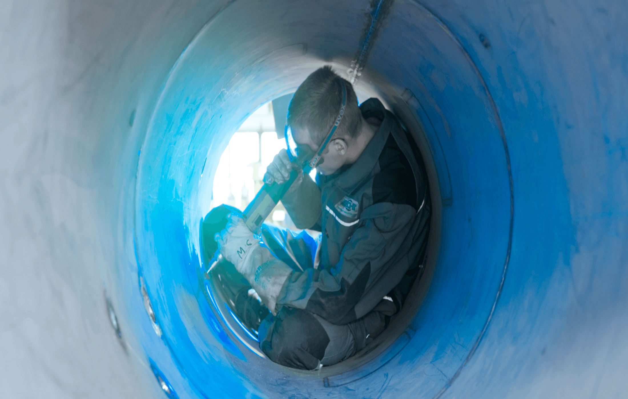 Ein Arbeiter in Schutzkleidung arbeitet im Inneren eines großen, blauen Rohrs.