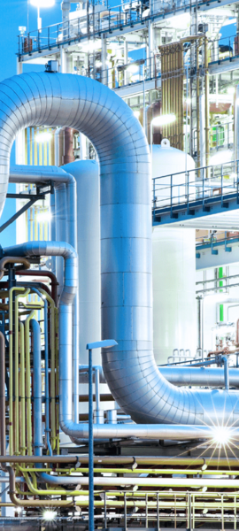 Beleuchtete Industrieanlage mit großen Rohren und Metallstrukturen in der Dämmerung.