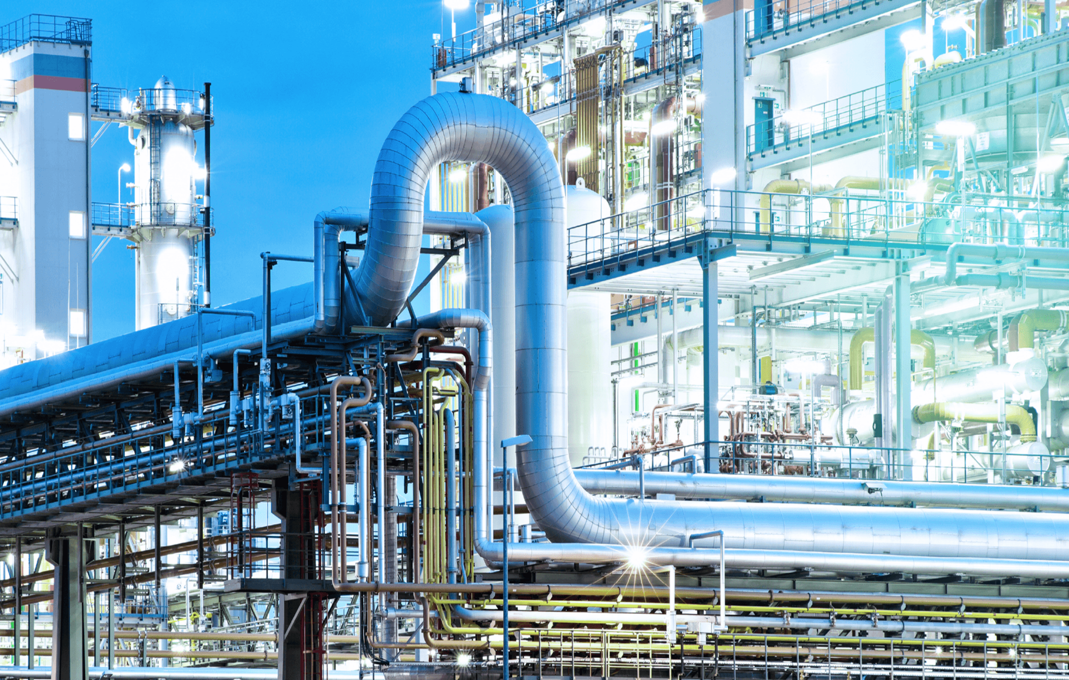 Beleuchtete Industrieanlage mit großen Rohren und Metallstrukturen in der Dämmerung.