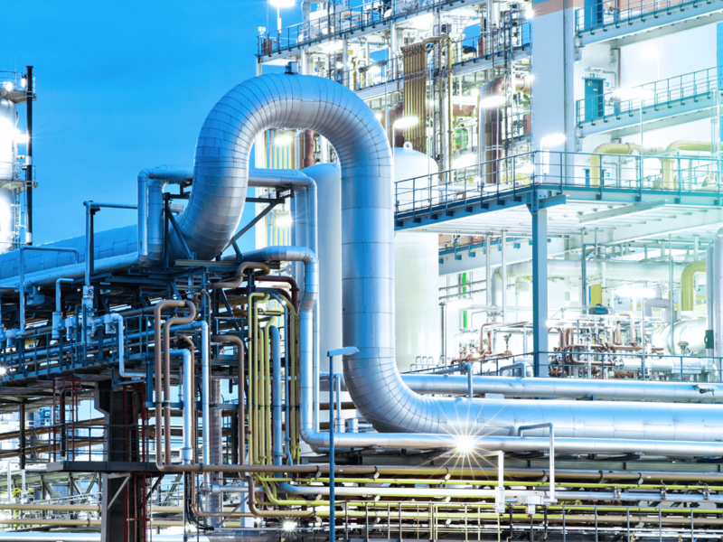 Beleuchtete Industrieanlage mit großen Rohren und Metallstrukturen in der Dämmerung.