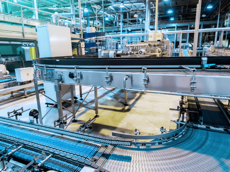 Moderne Förderbänder und Maschinen in einer industriellen Produktionshalle mit bläulicher Beleuchtung.