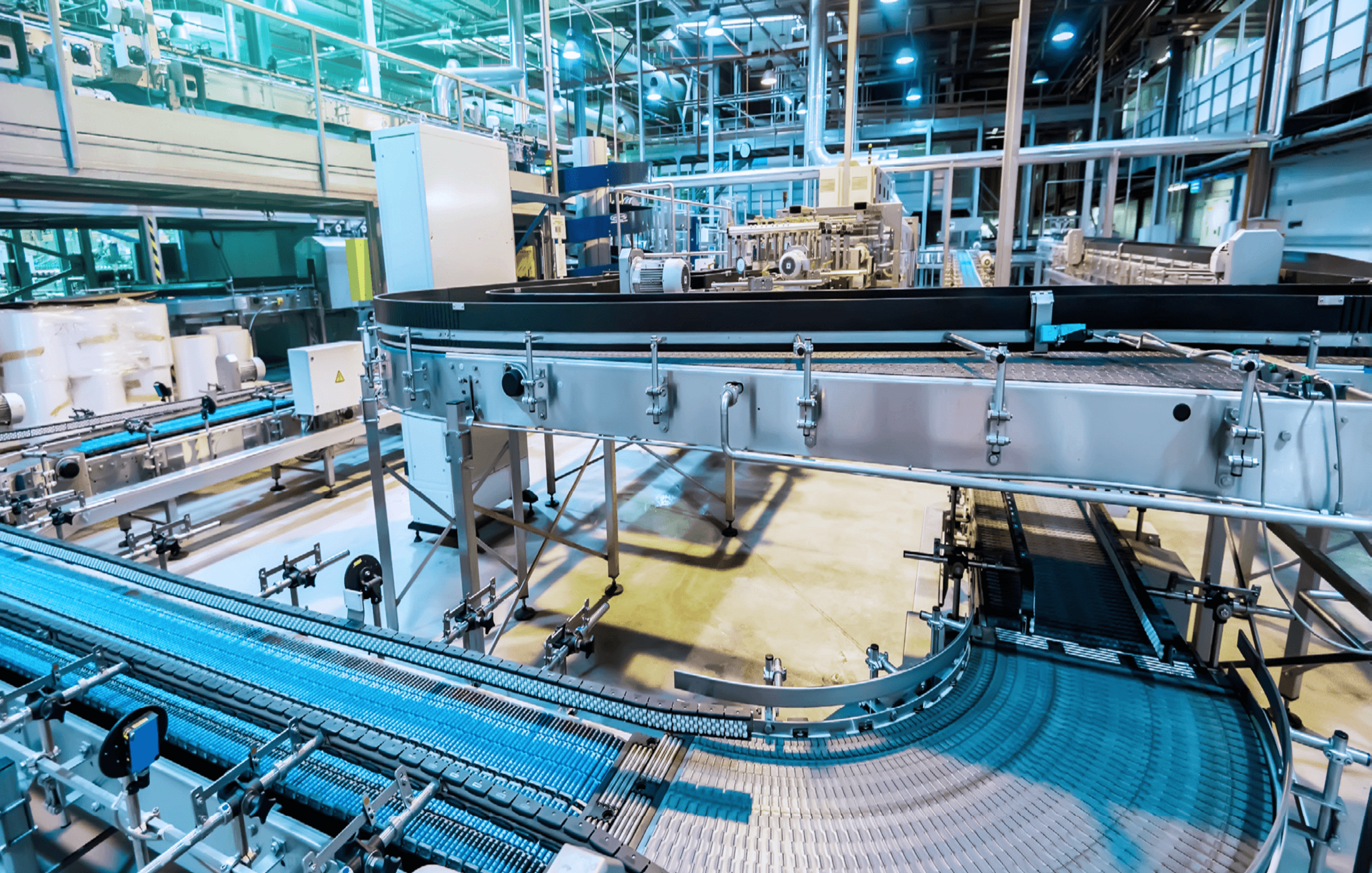 Moderne Förderbänder und Maschinen in einer industriellen Produktionshalle mit bläulicher Beleuchtung.
