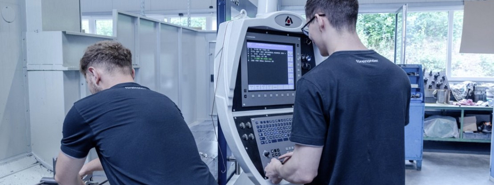 Two trainees working focused on a modern CNC milling machine in an industrial workshop.