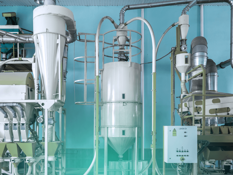 Komplexe Maschinerie einer Getreidemühle mit Rohren und Silos in einer Produktionshalle.